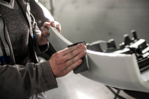 Car repair technician using a sanding paper to remove excess filling form a car bumper that got damaged in accident Body repair technician removing excess filling from an accident-damaged car bumper using a sanding paper. door panel stock pictures, royalty-free photos & images