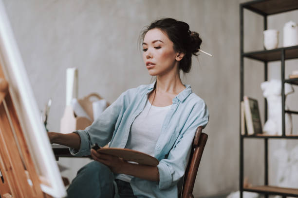 istock Concentrated young lady looking at the canvas while drawing 1135519726