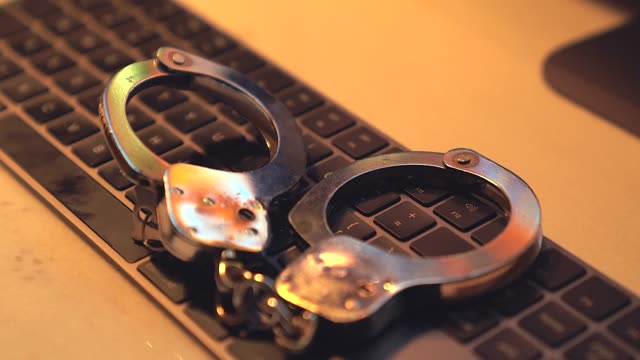 Cybercrime concept. Panning shot of Metal handcuffs putting on the computer keyboard.