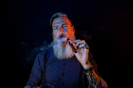 Portrait of a bearded man with a cigar in a blue and red light