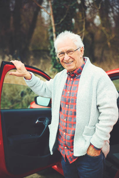 old friendly gentleman gets out of his car and smiles at the camera - old men car vertical imagens e fotografias de stock