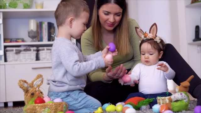 Mother with kids sitting on the floor and playing with Easter egg