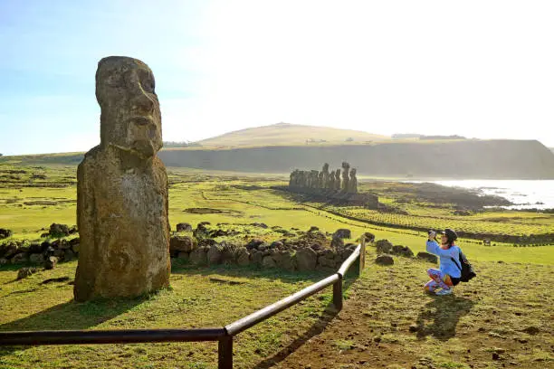 Photo of Female tourist taking photo of solitary Moai near the famous 15 Moais on the platform of Ahu Tongariki, Easter Island, Chile