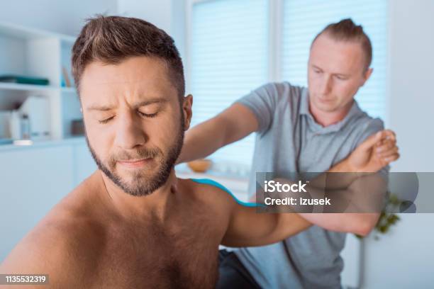 Physiotherapist Stretching Shoulder Of Young Man Stock Photo - Download Image Now - Adhesive Tape, Adult, Adults Only