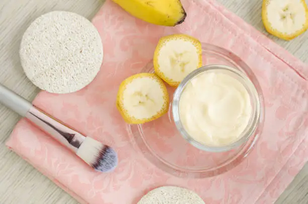 Photo of Homemade banana face mask (cream) in the small glass jar and cosmetic brush. DIY beauty treatments and spa. Top view, copy space.