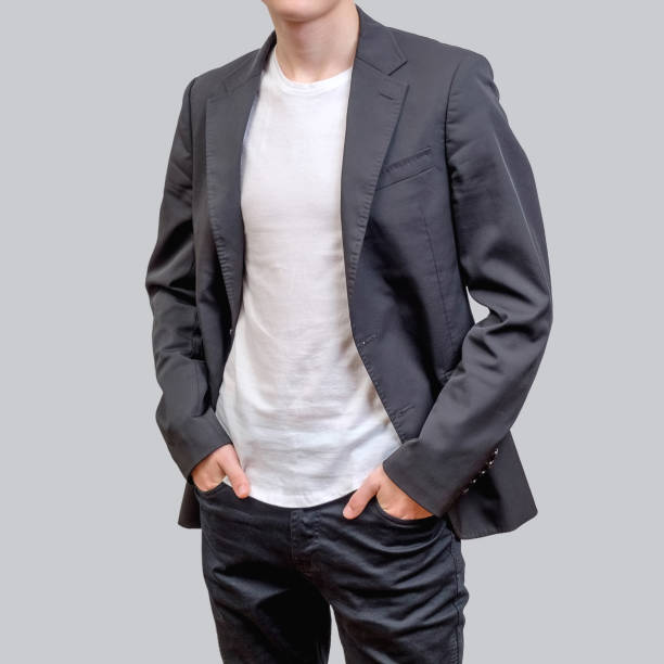 модный молодой человек в сером пиджаке и темных джинсах, стоящий на сером фоне. - blazer стоковые фото и изображения