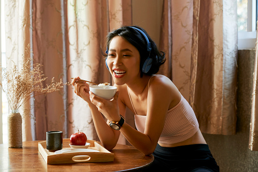 Cheerful young Asian woman enjoying tasty healthy breakfast at home