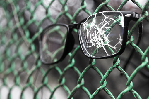 Close up of broken glasses on a metal lattice. concept of prison arrest or imprisonment.