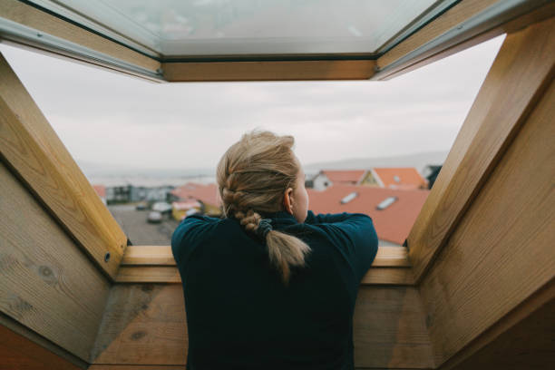 mujer mirando nuestra de la ventana en la ciudad - roof house residential structure window fotografías e imágenes de stock