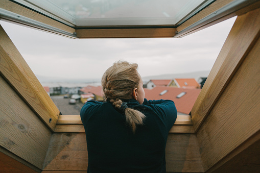 Young Caucasian woman looking our of the window on city on Faroe Islands