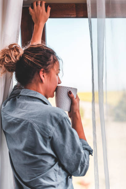 istock Young woman looking through the window with a cup 1135547090