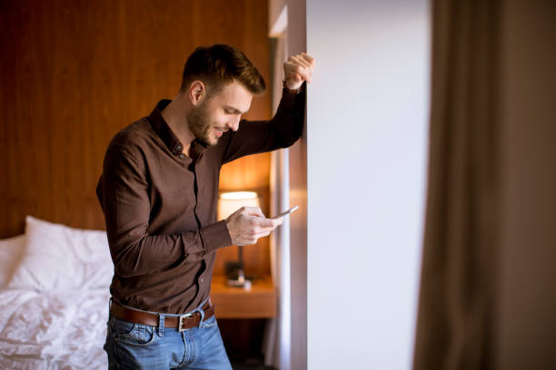 istock Young man using mobile phone in the room by window 1135547399