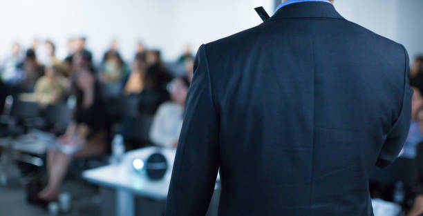 "Speaker on Stage at Conference Meeting Event. Presenter at Business Seminar Photo. Audience Watching a Manager Presentation. Blurred Image of Lecturer Presenting To Audience During Speech. " stock photo