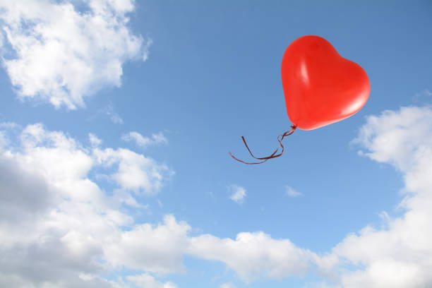 istock red heart shaped balloon flies into the blue sky with clouds, love concept, copy space 1135552325