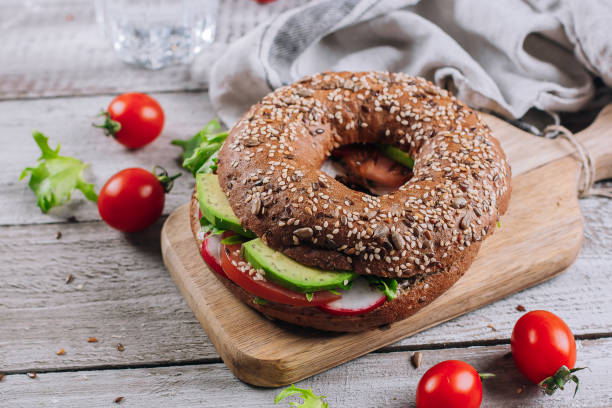 bagels com creme, abacate, tomates, rabanete e folhas verdes no fundo de madeira da placa e da tabela. comida saudável para o café da manhã. conceito equilibrado delicioso do alimento. vista superior e espaço da cópia - bun sandwich vegetable cream cheese - fotografias e filmes do acervo