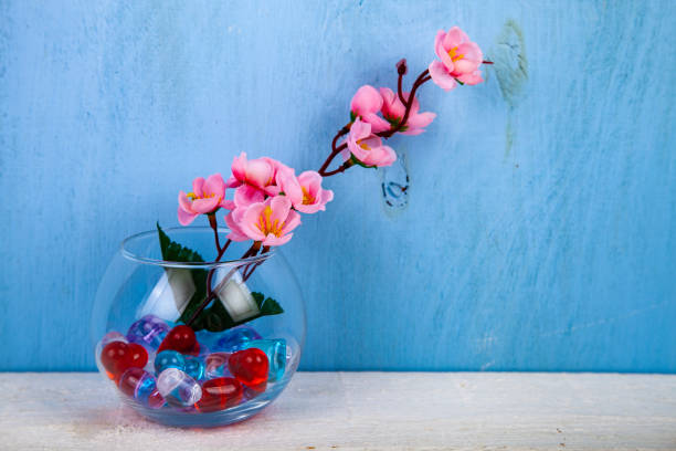 Multicolored glass hearts in a round vase and flowers on a blue background.