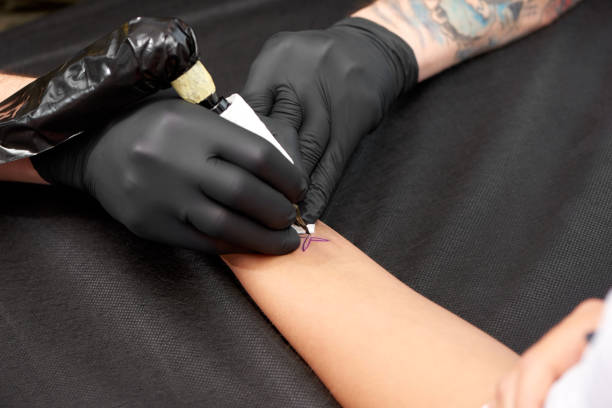 istock Master in black gloves beating tattoo on client's skin. 1135560200
