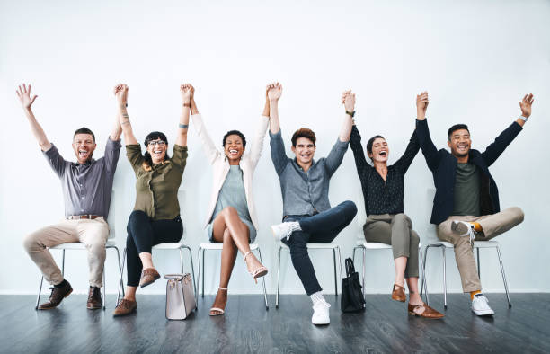 Showing up makes us all winners! Studio shot of a group of businesspeople holding hands and cheering in a waiting room passion stock pictures, royalty-free photos & images
