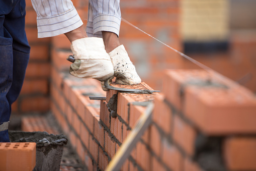A builder lays bricks wall on a rope with trowel