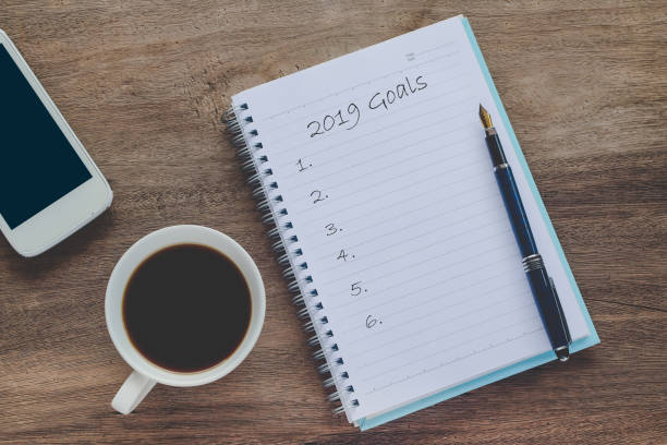 istock 2019 goals text on book note with cup of coffee, pen and smartphone. 1135566599