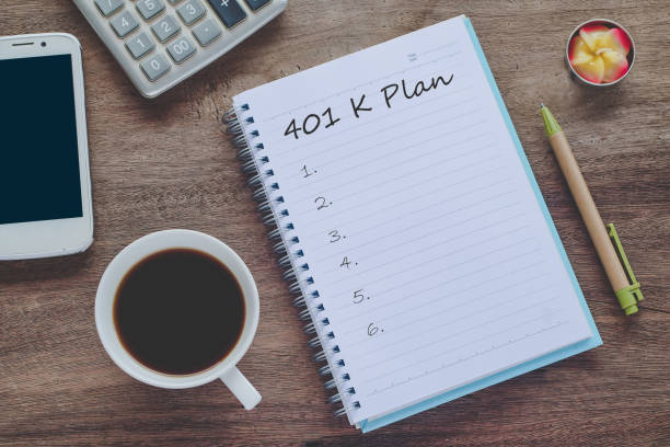 istock 401K Plan text on book note with cup of coffee, pen and smartphone. 1135566603