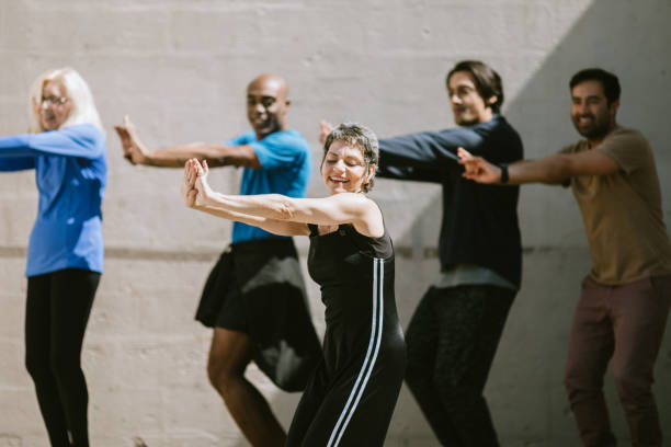 Diverse Outdoor Multigenerational Dance Class Group A group of friends of varying ages and ethnicities enjoys an exercise dance class outdoors at a park in Los Angeles.  A Hispanic woman leads the group in the steps and movements. dance troupe stock pictures, royalty-free photos & images