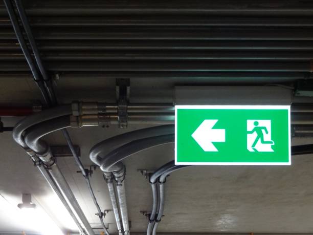 istock Green bright emergency fire exit with arrow show direction against metal electric wire pipe 1135571941