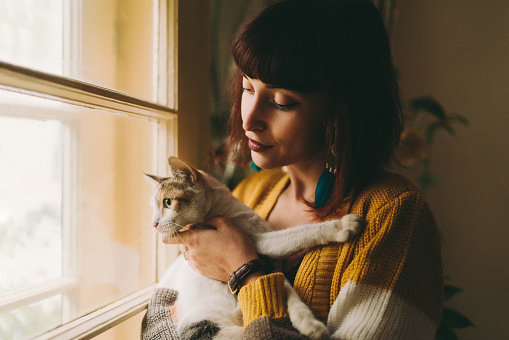 Young woman with cat staring through the window