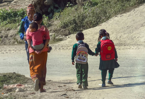 Everyday life in Nepal, children in uniform walk hand in hand to school, mother carries a small child on her back. stock photo