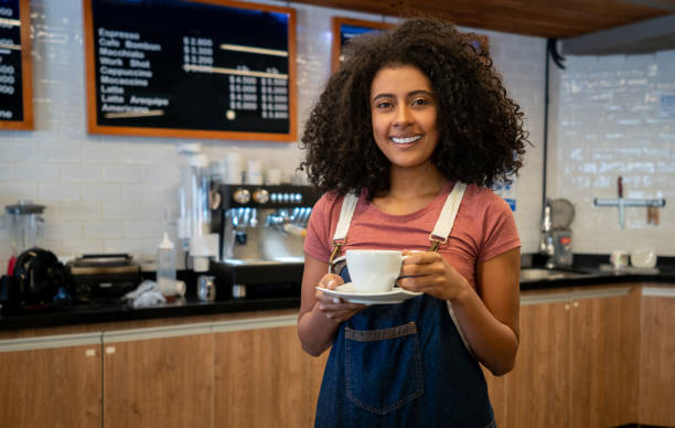 istock African american beautiful waitress at a coffee shop holding a mug while facing camera smiling 1135573719
