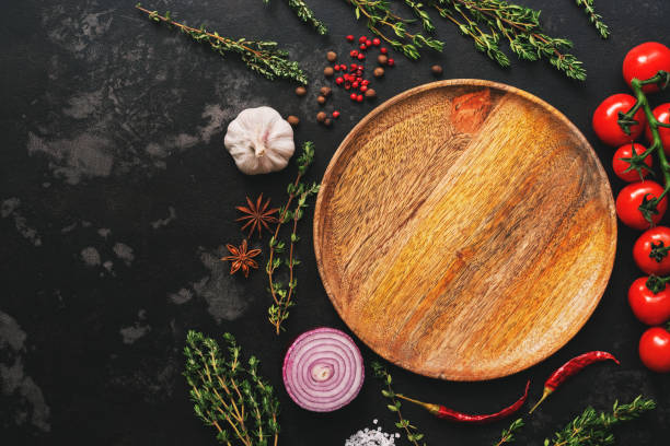 istock Flat lay empty wooden plate, vegetables, spices and herbs on dark stone background. Top view. 1135579302
