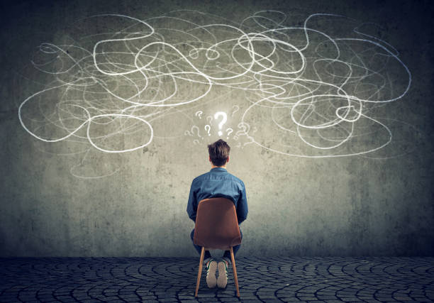 businessman sitting on chair looking at a scribble on a wall feeling confused Back view of a thoughtful young businessman sitting on chair looking at a scribble on a wall feeling confused with too many questions chaos stock pictures, royalty-free photos & images