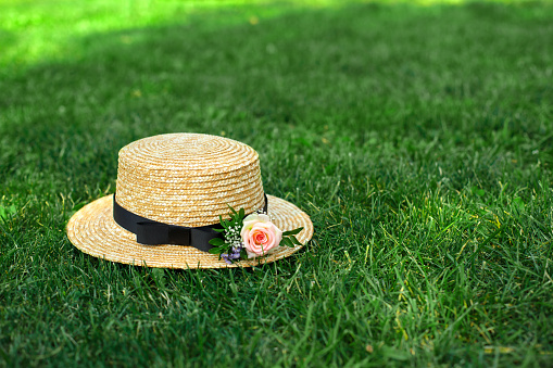 stylish straw hat with fresh flowers lay on a green lawn.