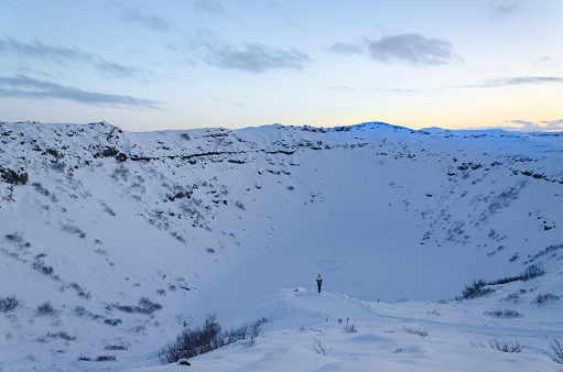 A woman inside Kerid Crater, at sunset, looking at a heart shape in the snow