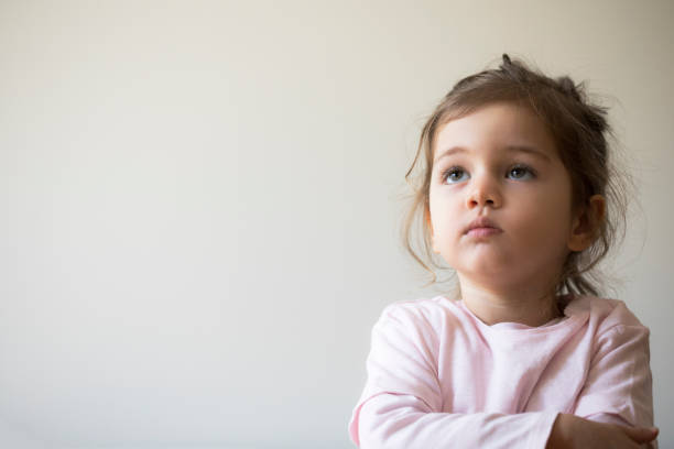 Serious Toddler Serious child with crossed arms is looking up in front of white wall. 4 year old girl stock pictures, royalty-free photos & images