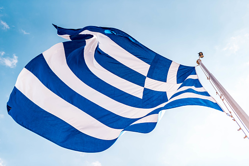 Greek flag floating in the air under the blue cloudy sky.