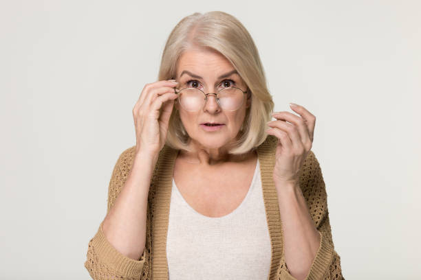 Shocked old woman in disbelief lowering glasses looking at camera Shocked old mature woman in disbelief lowering glasses looking at camera, surprised stunned amazed senior mid aged lady grandma peering feeling astonished isolated on grey white studio background grandma portrait stock pictures, royalty-free photos & images