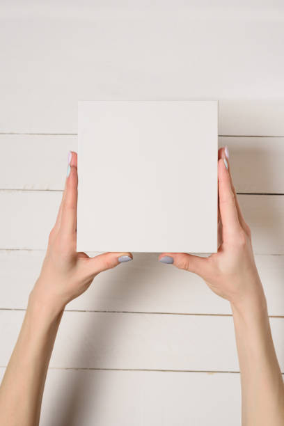 istock Small white cardboard box in female hands. Top view. White table on the background 1135587926