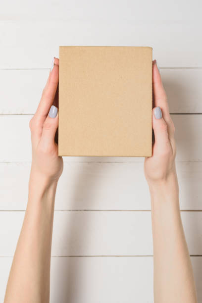 istock Small cardboard box in female hands. Top view. White table on the background 1135587927