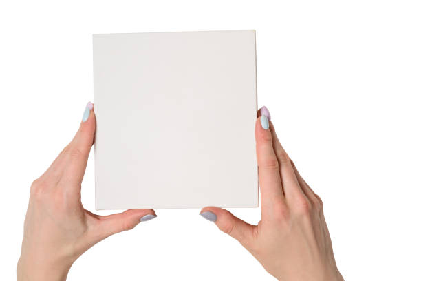 istock Small white cardboard box in female hands. Top view. White table on the background. Isolate 1135587967