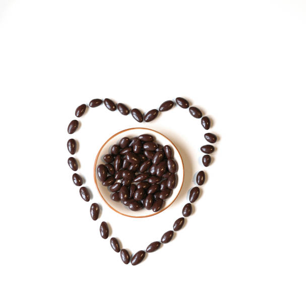 istock Nuts arranged in heart shape on background. Food image close up candy, chocolate milk, extra dark almond nuts. Love Texture on white grey table top view 1135588266