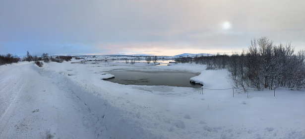 View of snowed road and a lake in Thingvellir National Park with a very low winter morning sun.