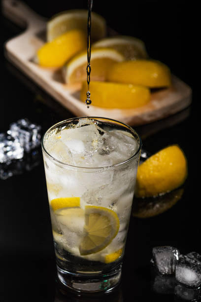 Pouring Sparkling cold water detox with lemon slices and ice on a dark glass background with black back