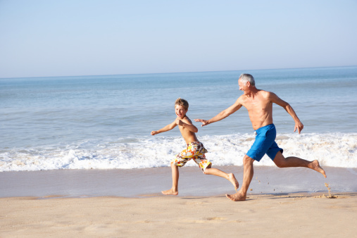 Grandfather having fun chasing grandson on beach