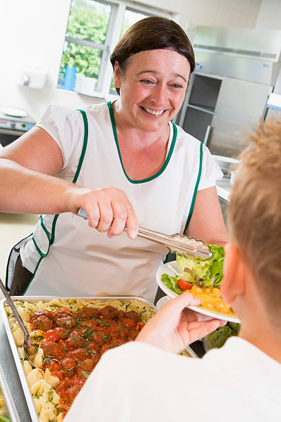 lunchlady bietet teller mit essen in der cafeteria der schule - kantinenfrau stock-fotos und bilder