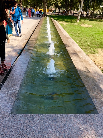 India Gate, New Delhi, India - March 10, 2019: Crowds of tourists viewing the modern India Gate fountain located in the surrounding India Gate lawns and park, New Delhi, India.