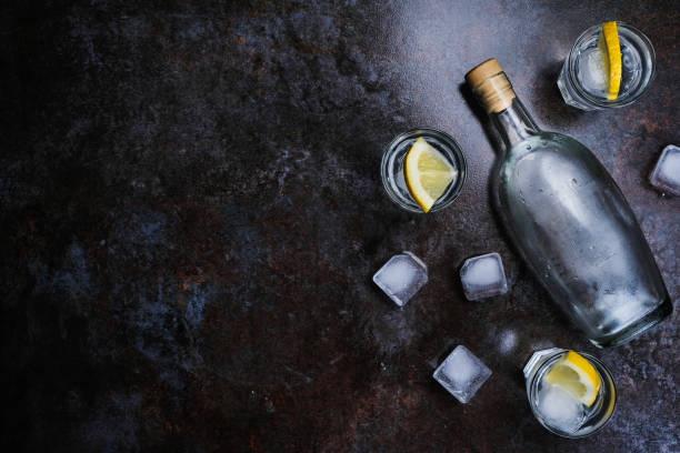 Cold vodka in shot glasses with lemon on stone background. Top view, copy space.