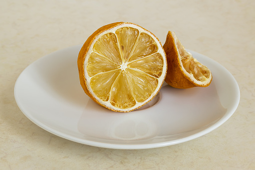 Lemon dried in the fridge. Stale citrus on a white saucer. Foods forgotten in the home refrigerator.
