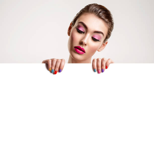 Beautiful woman with a colored manicure holds blank poster. Beautiful woman with a colored manicure holds blank poster. Attractive white girl with empty billboard. Glamour fashion model's holding placard, free space. Fashionable advertisment concept. Art person holding frame over face stock pictures, royalty-free photos & images