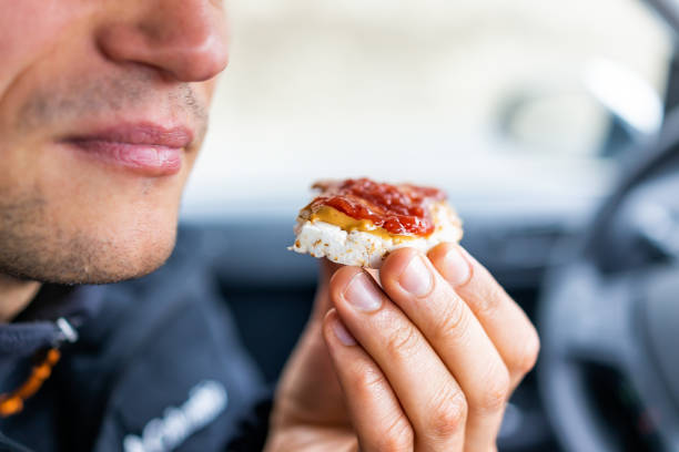 Macro closeup of man hand holding one rice cake by mouth in car road trip blurry background topped with peanut butter, strawberry jam as vegan dessert snack Macro closeup of man hand holding one rice cake by mouth in car road trip blurry background topped with peanut butter, strawberry jam as vegan dessert snack biscuit quick bread photos stock pictures, royalty-free photos & images